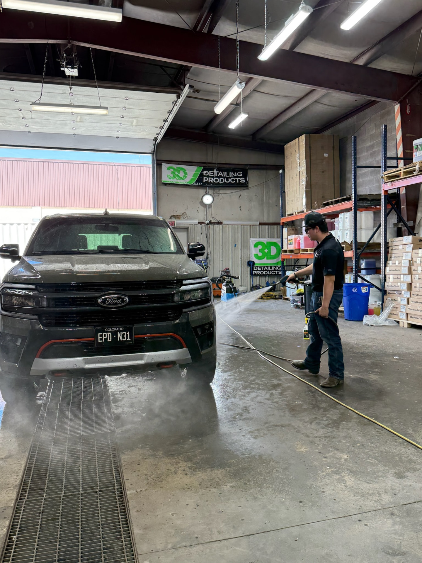 Technician rinsing the front of a dusty Ford Expedition in the wash bay